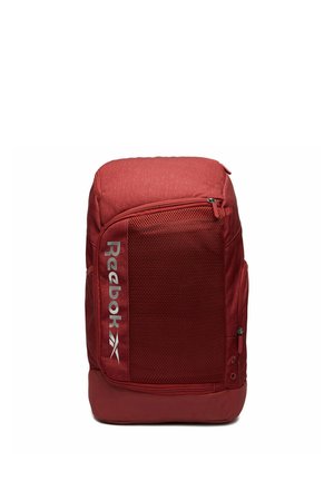 Czerwony plecak Reebok z przednią siatkową kieszenią i pionowym, oznakowanym logo, zamkami błyskawicznymi po bokach i na górze, o strukturalnym, prostokątnym kształcie.