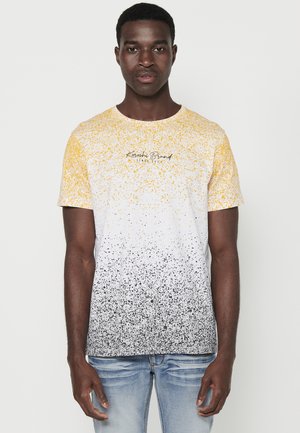 La t-shirt a maniche corte presenta un design a gradiente che va dal giallo al bianco al nero. Sfere tessurate su tutta la superficie. Tessuto morbido. Vestibilità comoda.