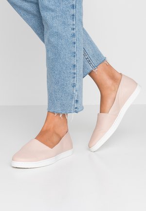 Helle rosa Slipper aus strukturiertem Material mit weißer Sohle, kombiniert mit zerrissenen blauen Jeans.