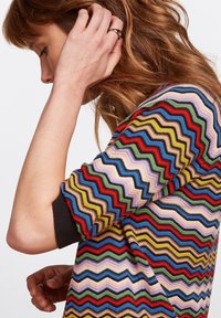 dzianinowy top z wielokolorowym wzorem zygzakowym w różnych odcieniach, z czarnym ściągaczem. Teksturowany materiał, prezentujący żywe kolory.