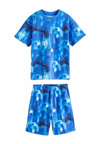 Ensemble chemise manches courtes et shorts bleus avec impression numérique de manettes de jeu et ballons de football sur un fond bleu flou.
