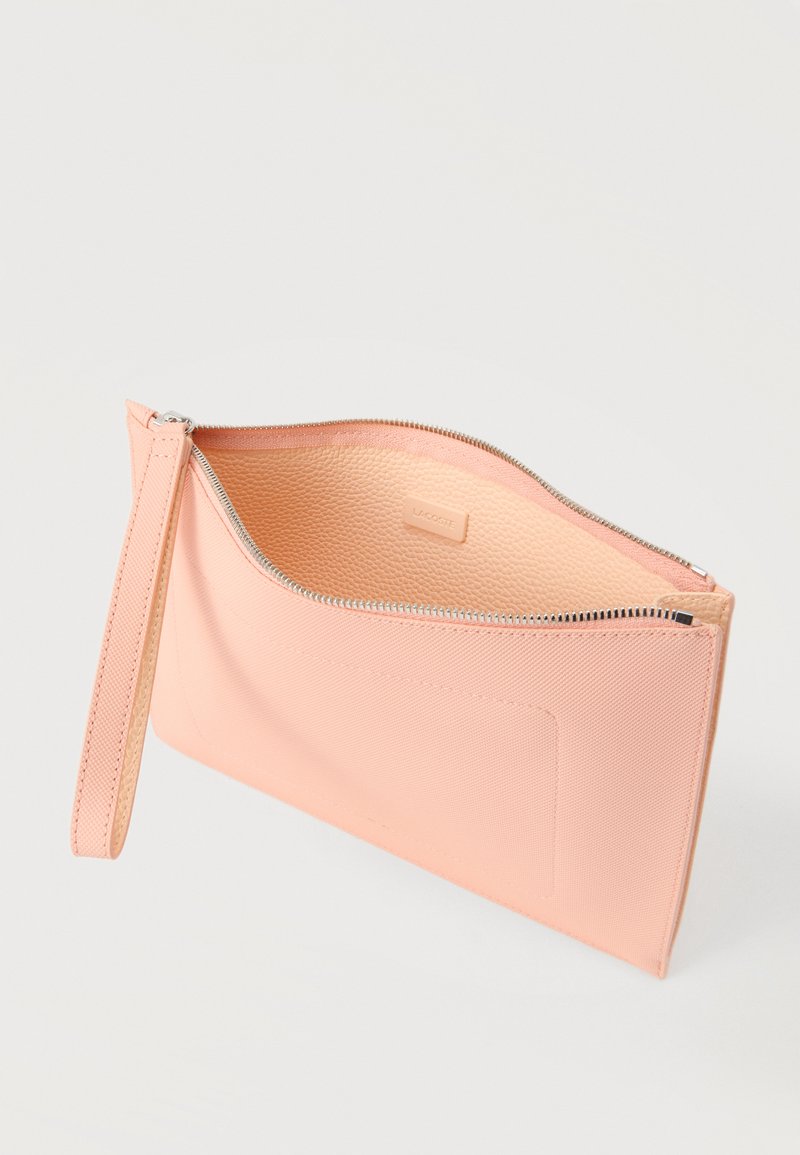 Zachtroze polstasje met zilveren ritssluiting, gestructureerde binnenkant en afneembare band, deels open weergegeven tegen een lichte achtergrond.