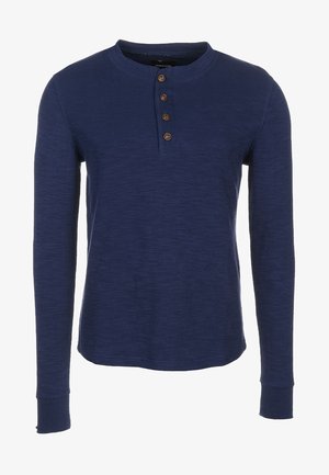 Chemise henley à manches longues bleu marine avec quatre boutons marron et un col rond.