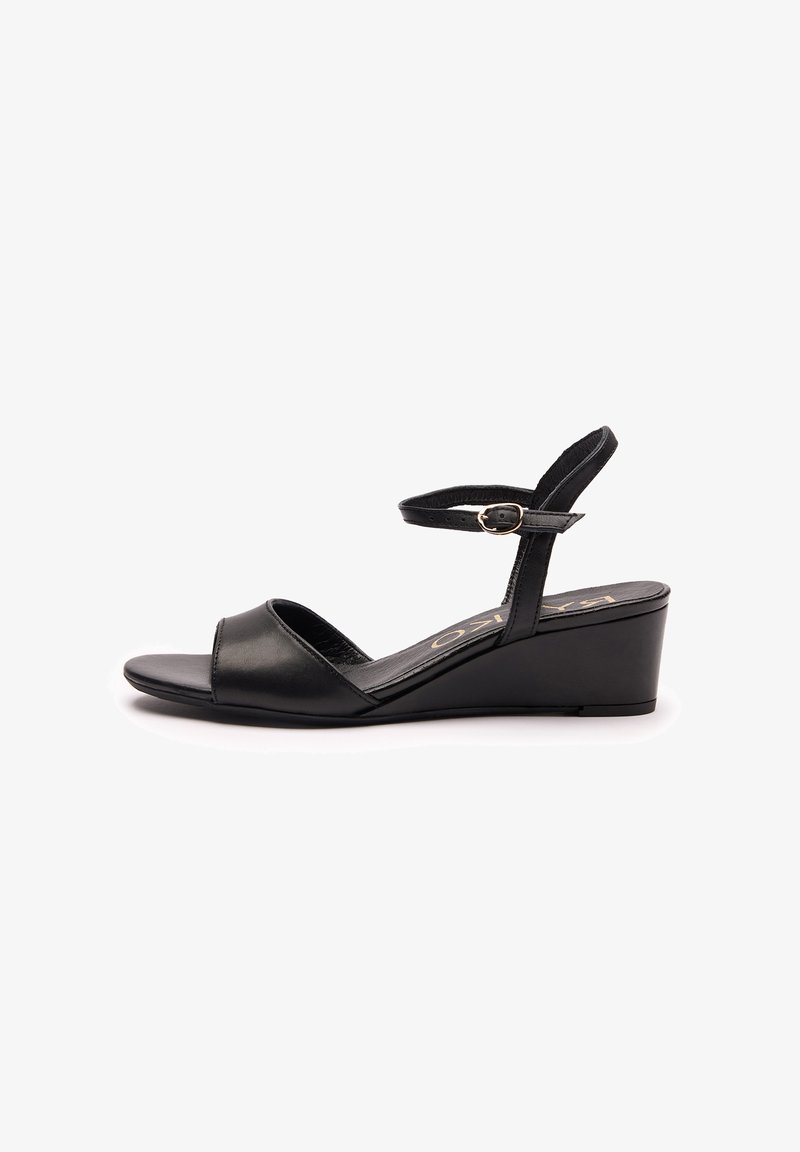 Sandales compensées noires en cuir lisse, avec bout ouvert et bride autour de la cheville ornée d'une boucle dorée. Talon compensé bas.