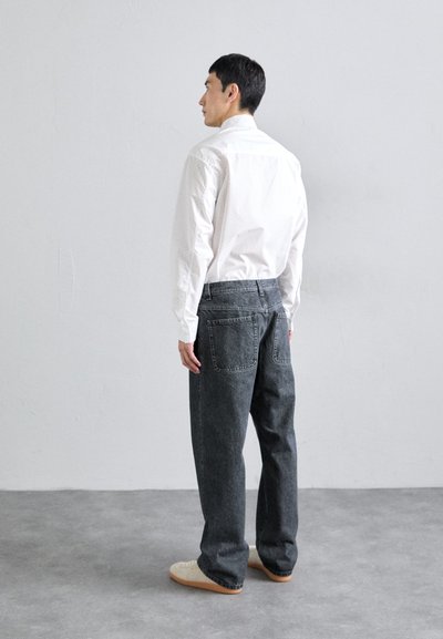 Grå denimjeans med avslappnad passform och två bakfickor, tillsammans med en vit skjorta med knappar. Klädseln kompletteras med beiga skor.