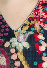 Prenda con escote en V y un estampado floral en colores vibrantes, que presenta un acabado plateado a lo largo del escote. Textura suave, diseño detallado.