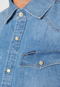 Ljusblå denimskjorta med klassisk krage, metallknappar, bröstficka och en liten G-Star-logotag. Texturerat tyg.