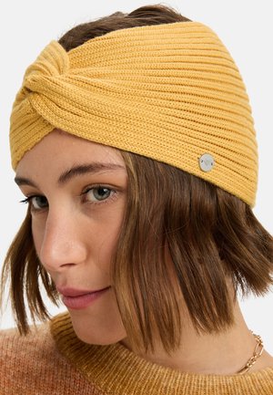 Gehaakte gele hoofdband met een draai ontwerp aan de voorkant, voorzien van een geribbelde textuur en een klein zilveren logo accent.
