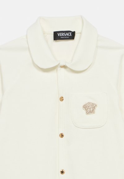 Κρεμ πόλο μπλουζάκι με γιακά, χρυσά κουμπιά και μικρό κεντημένο λογότυπο  στη τσέπη στο στήθος. Μαλακή υφή.