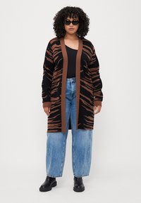 Cardigan a rayas negras y marrones, diseño de frente abierto, bordes acanalados, combinado con jeans azul de talle alto y botines negros.