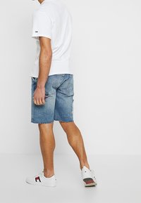 Vit kortärmad t-shirt och blå denimshorts. Shortsen har en urtvättad look, lätt slitningar och en bakficka med accentdetaljer. Vita sneakers.