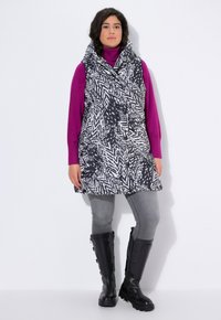 Zwart-wit gestreepte vest met een oversized kraag, laag over een paarse coltrui, gecombineerd met grijze legging en zwarte kniehoge laarzen.