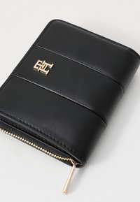 Black leather wallet with a zip closure and a gold logo accent. Features horizontal stitching and a textured surface.