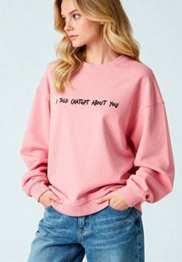 Felpa rosa in misto cotone con colletto tondo, spalle scese e testo nero che legge "HO PARLATO DI TE A CHATGPT". Abbinata a jeans blu.