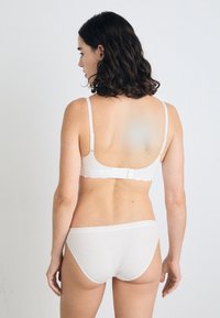 Ensemble de lingerie blanche avec un design festonné sur le soutien-gorge et la ceinture, texture lisse, bretelles ajustables et fermeture à crochets.