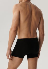 Czarne elastyczne bokserki z bezszwowym wykończeniem. Na modelu widoczny jest nagi plecy, ukazujące gładką skórę i wysportowane mięśnie.