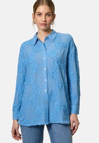 Light blue button-up shirt with textured floral patterns, long sleeves, and a collar. Smooth fabric and a relaxed fit.