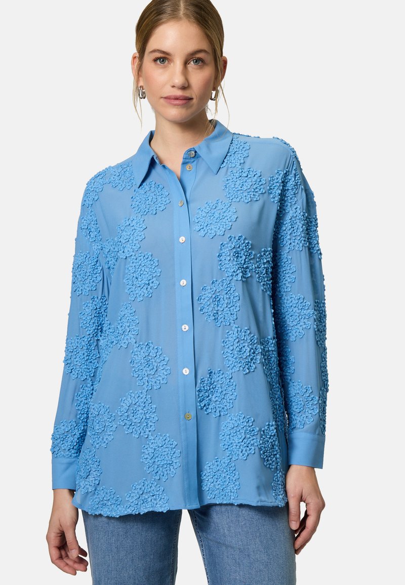 Light blue button-up shirt with textured floral patterns, long sleeves, and a collar. Smooth fabric and a relaxed fit.