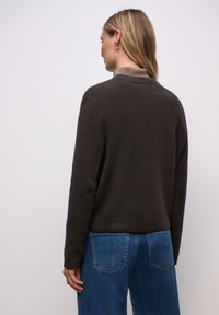 Tmavě hnědý svetr s texturou a límcem, ve volném střihu, doplněný modrými džínami. Svetr má žebrované manžety.