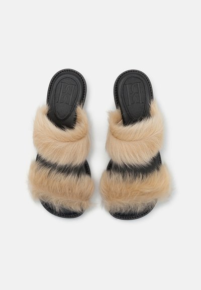 Faux fur sandals featuring black soles, two wide tan and light brown fuzzy straps, and embossed branding on the footbed.