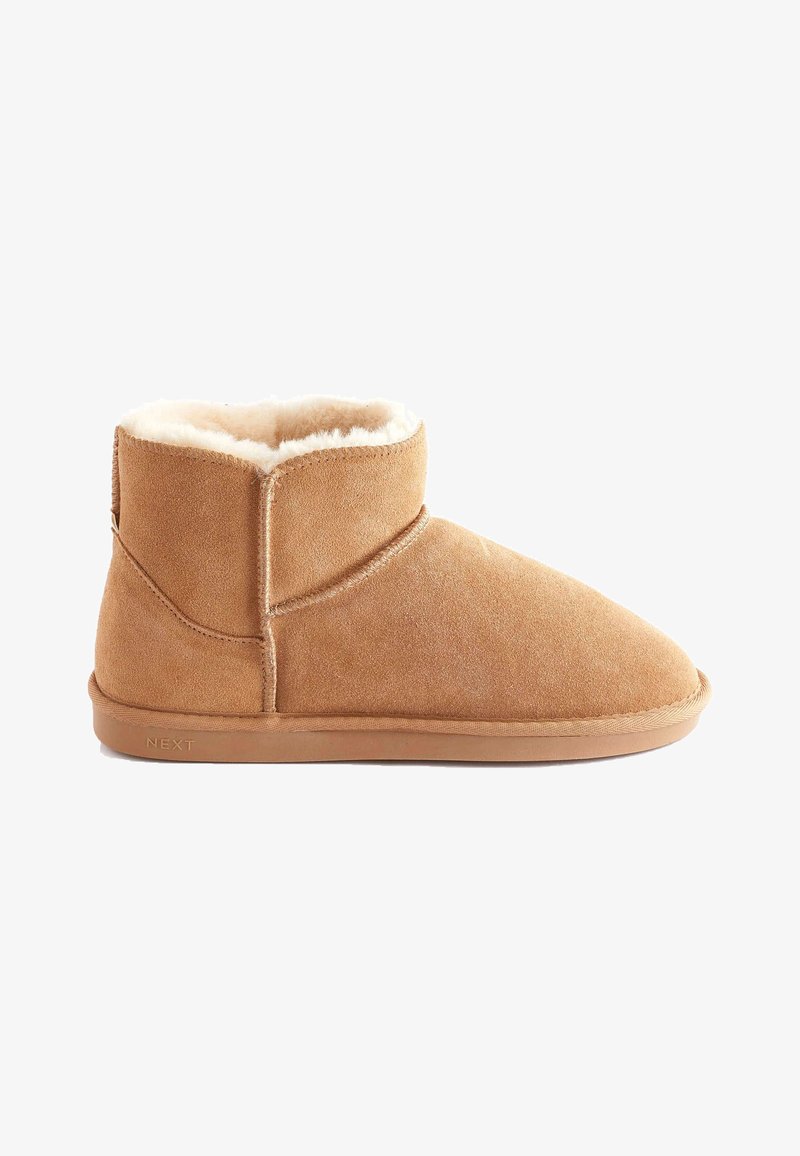 Tan suede ankle boot with a rounded toe, plush white lining, and a smooth rubber sole. Features a stitched design and brand label.