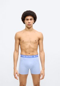 Ανοιχτό μπλε αντρικά μποξέρ με μπλε μέση και το λογότυπο "BJÖRN BORG" τυπωμένο. Λείο ύφασμα και εφαρμοστή σχεδίαση. Το μοντέλο εμφανίζεται όρθιο.