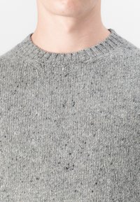 Gray knitted sweater with a ribbed crew neck. Texture is soft and speckled with lighter flecks. Fabric appears thick and warm.