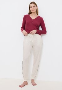 Bordeaux lange mouw henley shirt met knoopdetails, gecombineerd met lichtbeige sweatpants met een trekkoord en zijstrepen.