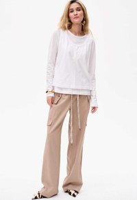 Weißes Langarmoberteil mit rundem Halsausschnitt, kombiniert mit beigefarbenen, weiten Cargo-Hosen mit Taschen und einem gemusterten Kordelzug.