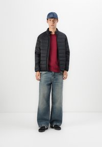 Sort dunjakke med lodret syning, maroon sweatshirt under, brede lyseblå denimjeans og en denimkasket. Sorte sko fuldender looket.