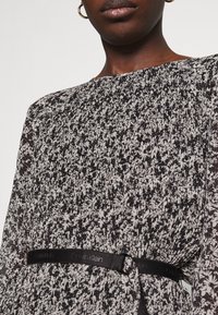 Zwart-witte bloemenpatronen jurk met lange mouwen, voorzien van een zwarte tailleband met een logo-accent en een gestructureerde stof.