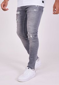 Harmaat farkku skinny-farkut, joissa on kulutettuja yksityiskohtia, useita revittyjä kohtia ja haalistunut pinta, yhdistettynä valkoisiin tenniskenkiin.