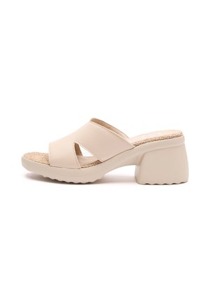 Beige slip-on sandal med to brede krydsede remme, en tekstureret vævet indersål og en chunky formet hæl med en bølget kant.