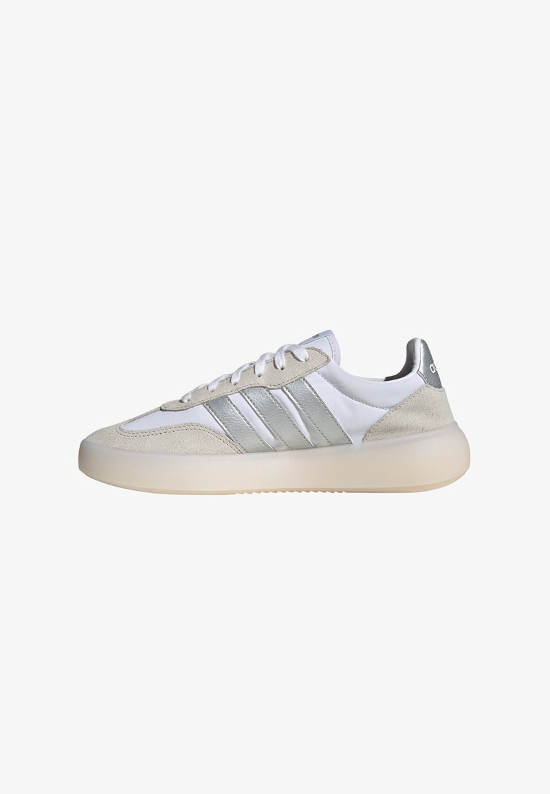 Scarpe sportive bianche e grigie realizzate in pelle scamosciata e materiali sintetici, con tre strisce argentate, una suola di gomma liscia e lacci piatti.