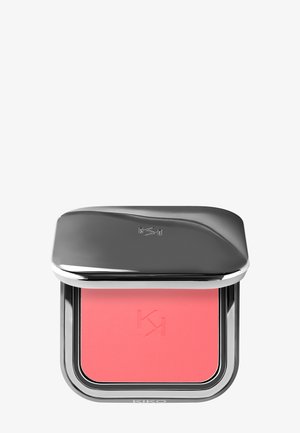 Blush compact dans un boîtier argenté. Comprend une poudre lisse de couleur corail rose et un logo embossé. Bords arrondis et couvercle incurvé réfléchissant.