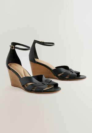 Sandales compensées noires avec un design de brides croisées, une lanière de cheville réglable et un talon en bois texturé. Empeigne et semelle intérieure en cuir lisse.