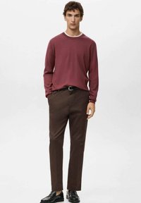 Bordowy sweter z dzianiny z prążkowanym dekoltem w zestawieniu z brązowymi spodniami o prostym kroju. Czarne lordsy dopełniają strój.