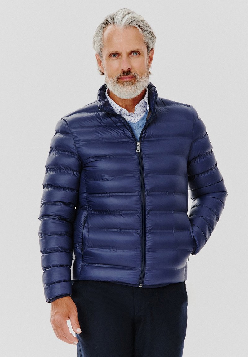 Granatowa kurtka puchowa z poziomym pikowaniem, wysokim kołnierzem i zapięciem na zamek, wykonana z błyszczącego, lekkiego materiału.