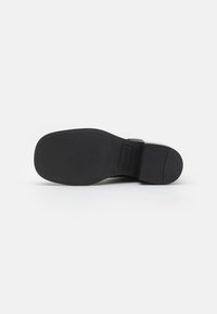 Black shoe sole with a smooth rubber finish, rounded heel, and slight tread pattern, featuring embossed brand logo on the side.