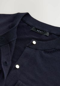 Navy blue cardigan made of soft fabric, featuring a ribbed neckline and gold-tone button detail near the collar. Label reads "NEXT."