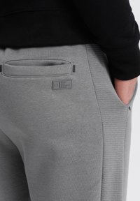 Graue Jogginghosen mit glatter Textur, gerippten Seiteneinsätzen und einer Gesäßtasche, die mit einem rechteckigen Logopatch versehen ist.