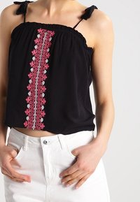 Top cropped nero con spalline regolabili, caratterizzato da un elaborato design ricamato rosa e argento al centro. Tessuto morbido.