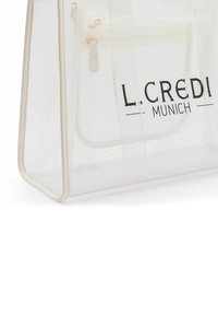 Sac cabas en mesh transparent avec des accents blancs subtils, équipé de ferrures dorées et du logo imprimé "L. CREDI MUNICH" sur le côté.