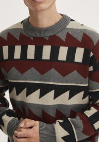 Sweater featuring a crew neckline, made of knit fabric. Geometric patterns in burgundy, gray, black, and cream. Textured ribbed cuffs.