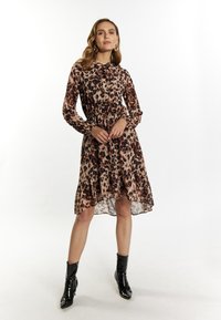 Langarmige jurk met dierenprint in beige, bruin en zwart, met een gerimpelde halslijn en een gelaagde zoom. Gecombineerd met zwarte enkellaarsjes.