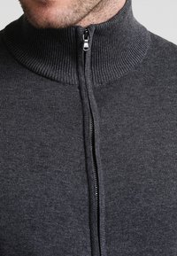 Tummanharmaa korkeakauluksinen villapaita vetoketjulla. Kauluksessa ja vetoketjussa resorikuviointi, pehmeä kangas ja istuva malli.