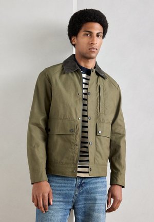 Olive green jacket with a corduroy collar, zip closure, and front pockets, worn over a striped t-shirt and blue jeans. Smooth texture.