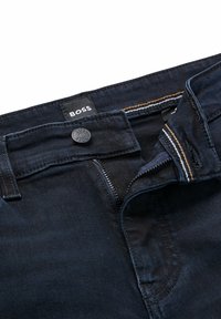 Dark denim jeans with a button closure and zipper. Features a "BOSS" label and contrasting yellow stitching on the waistband and pockets.