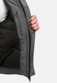 Interior de chaqueta gris con un suave forro negro, bolsillo con cremallera y cierres de botón, con una textura exterior lisa y aislamiento acolchado.