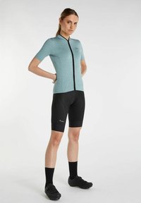 Maillot de vélo à manches courtes, couleur vert menthe, avec fermeture éclair sur le devant, associé à un short rembourré noir et des chaussures de cyclisme noires. Tissu lisse, coupe athlétique.